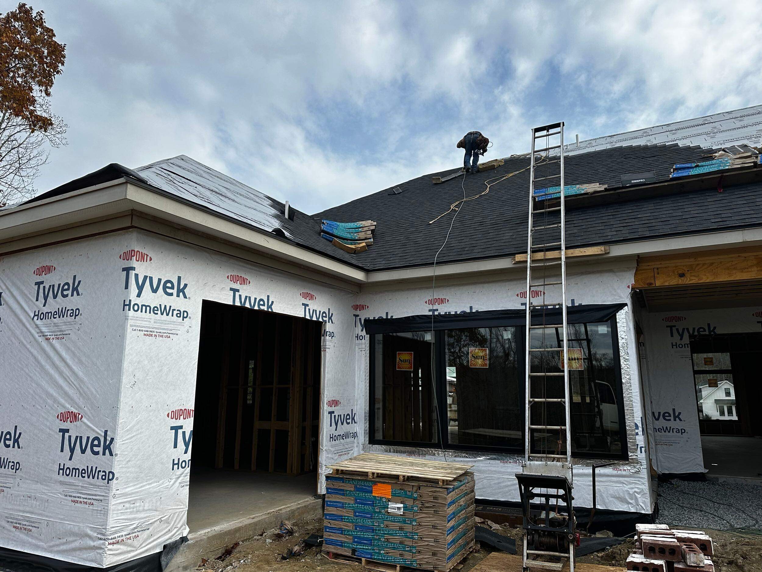 roof installation in progress with protective wrap on walls and materials organized at the job site for custom home construction