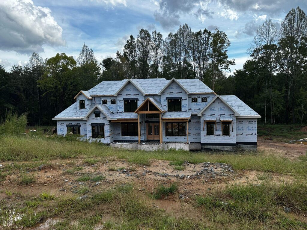 the image showcases the exterior of a custom home under construction featuring framing and windows being installed around a partially completed structure