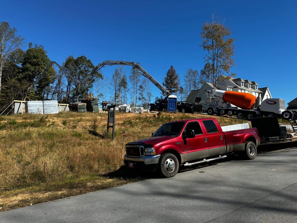 the image shows workers pouring concrete for a foundation at a custom home construction site with heavy machinery present