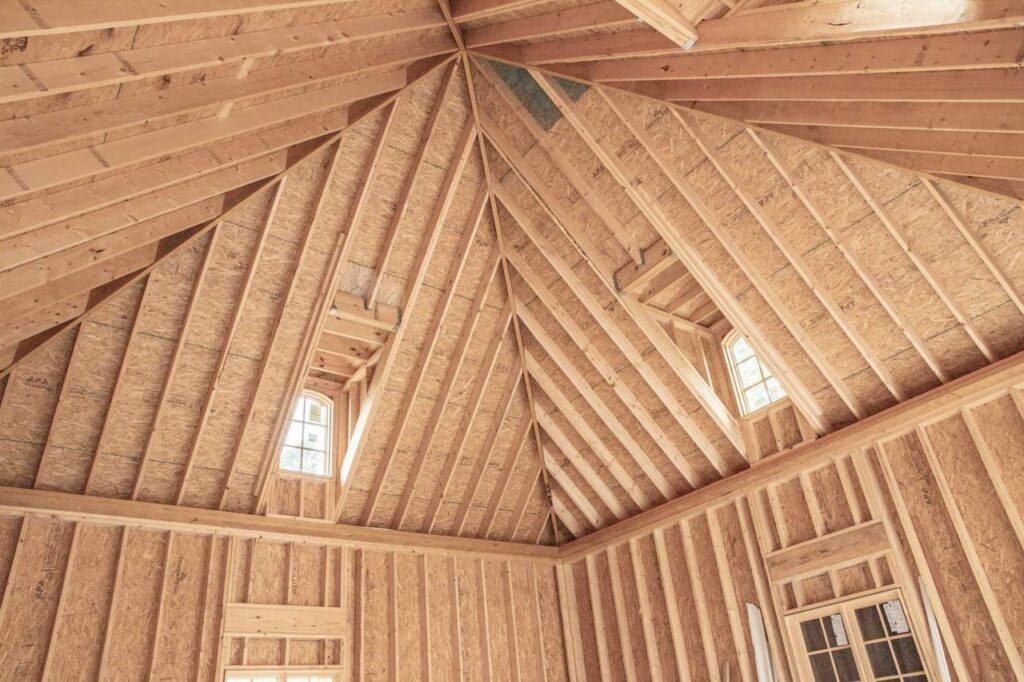 the photo shows a wooden frame of a vaulted ceiling in the process of construction with windows being installed